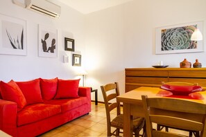 A red sofa, wooden dining table, chairs, and wall-mounted artwork.
