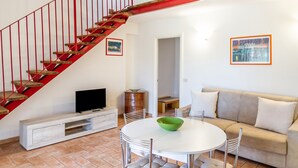 A living room with a red staircase, a white dining table, a beige sofa, and a television on a white cabinet.