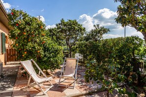 Un patio con dos sillones de descanso, una mesita y un jardín con árboles frutales y arbustos.