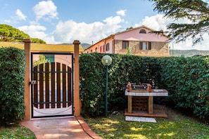 A gated entrance with a brick pathway leading to a building with a pink facade and stone accents. - Holiday Home "Palmiro" with Shared Garden & Wi-Fi (Castiglione della pescaia)