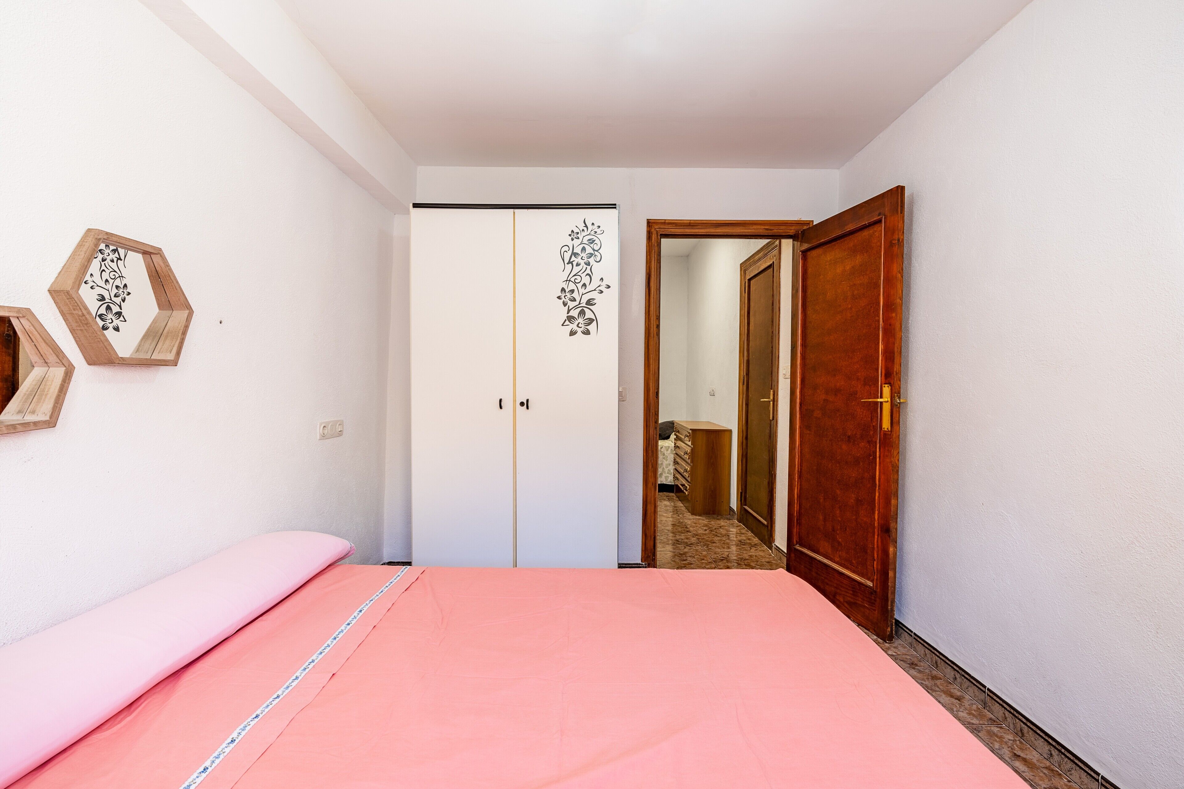 A bedroom with a bed, a wardrobe, a wooden door, and a hallway leading to another room.