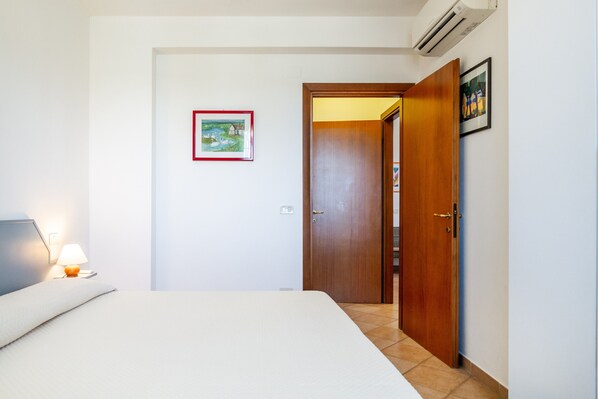 Un dormitorio con cama, mesita de noche, lámpara, puerta y un cuadro en la pared.