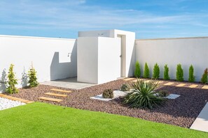 Ein moderner Außenbereich mit einer weißen Wand, einem kleinen Garten mit Kies, Pflanzen und einem Holzweg.