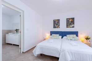 Ein Hotelzimmer mit Doppelbett, Nachttisch mit Lampe sowie Bad mit Waschbecken und Spiegel.