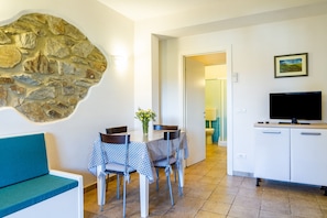 A dining area with a stone wall, a table with chairs, a sofa, a television, and a cabinet. - Apartment 'Casa Flavia' with Shared Garden and Wi-Fi (Castiglione della pescaia)