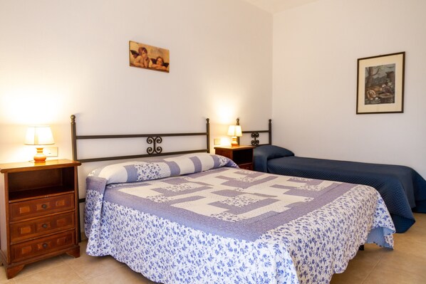 Un dormitorio con una cama, dos mesitas de noche, una lámpara y dos cuadros en la pared.