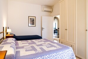 Une chambre à coucher comprenant un lit, une table de chevet, une lampe, une armoire et un appareil de climatisation.