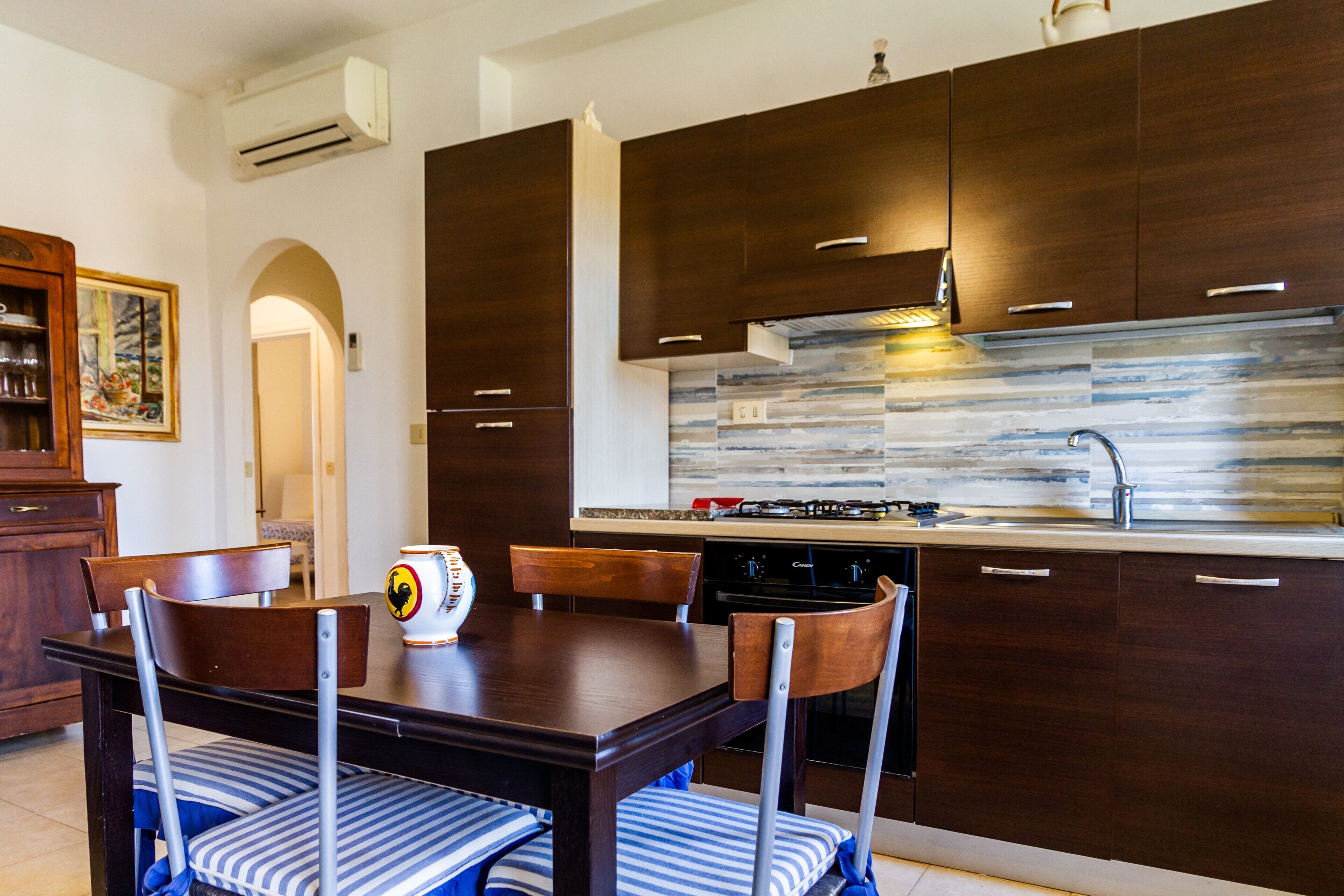 A modern kitchen with dark wood cabinets, a stainless steel backsplash, and a dining area with a wooden table and chairs.