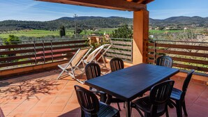 Une terrasse extérieure couverte, dotée d’une table et de chaises, qui offre une vue sur un paysage rural avec des collines et un ciel dégagé.