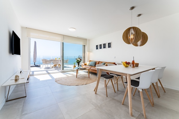 A modern living space with a dining area, sofa, and large windows overlooking the sea.