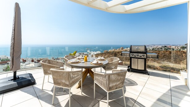 Une terrasse sur le toit avec une table ronde, des chaises en osier, un barbecue et une vue sur la ville et la mer.