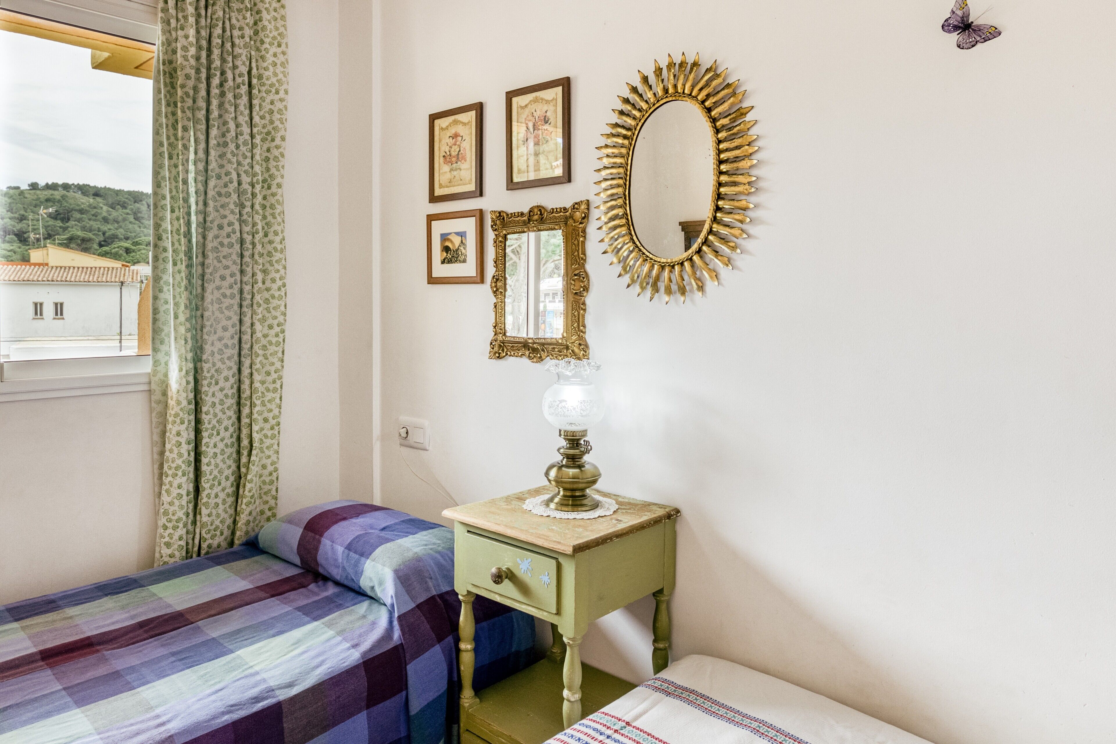 A room with two beds, a small table with a lamp, a mirror, and framed pictures on the wall.