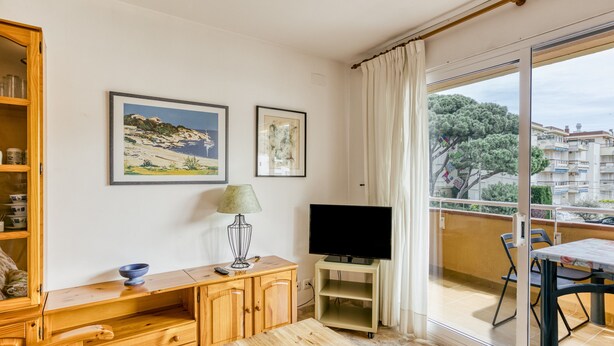 A room with a wooden desk, a television on a stand, a painting, and a balcony with a view of buildings. - Apartment 'Montgo' with Mountain View, Wi-Fi and Air Conditioning (L'Escala)