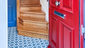 Un escalier avec des marches en bois menant à un palier, une porte rouge avec une poignée argentée, et une porte bleue en arrière-plan.