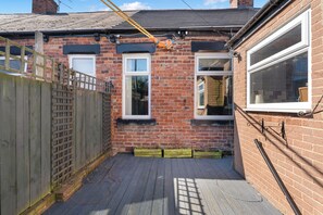 A brick house with two windows, a wooden fence, and a metal roof.