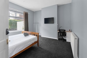 A bedroom with a bed, a desk, a chair, a television, and a window with curtains. - Sommerset Cottages (Sunderland)