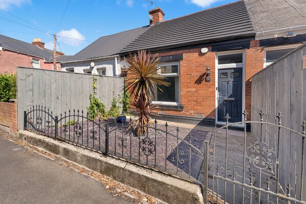 A residential house with a brick facade, a dark-colored door, and a metal fence with decorative elements.