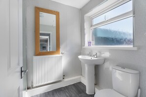 A bathroom with a white radiator, a sink, a toilet, and a window with frosted glass.