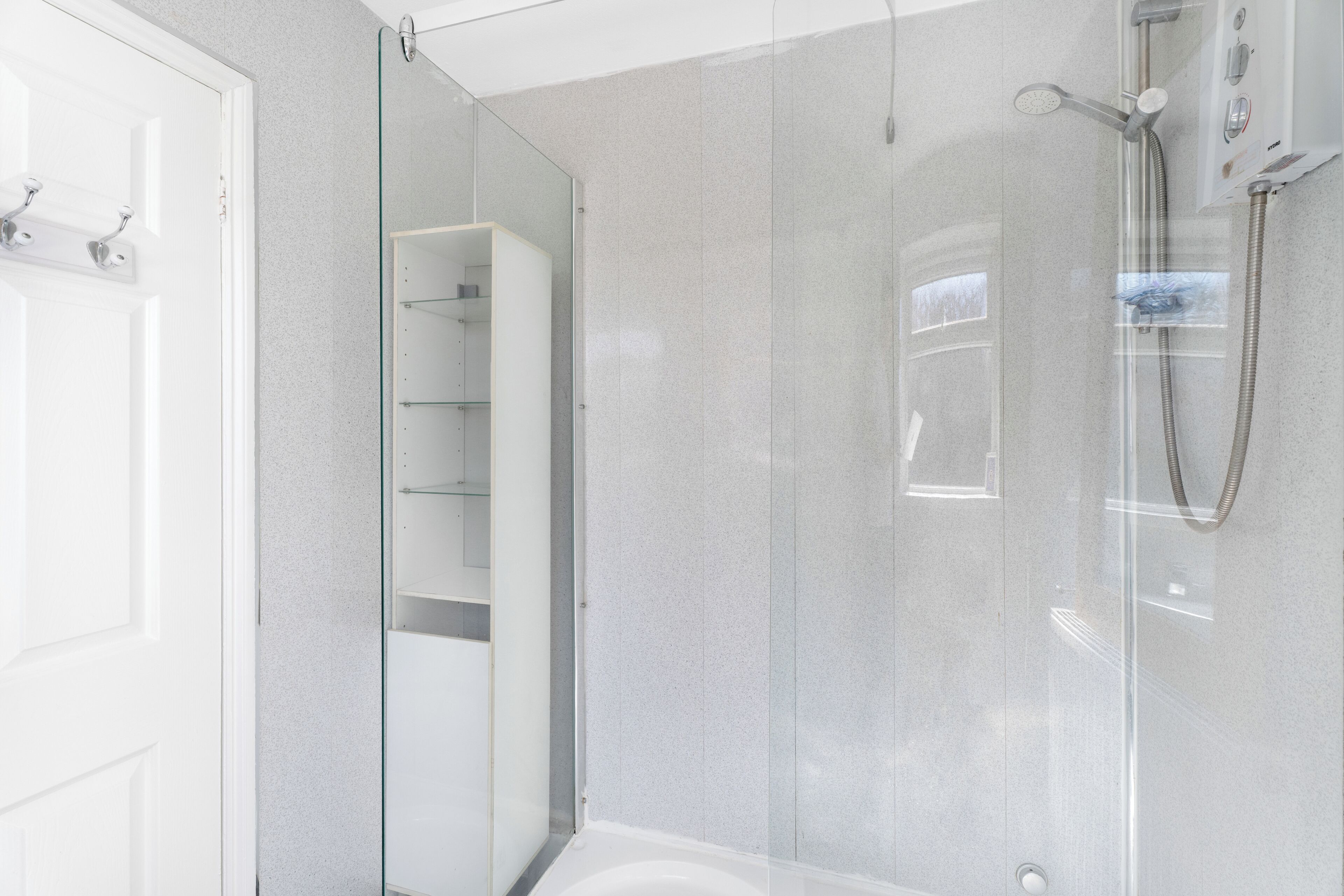 Un baño moderno con cabina de ducha de vidrio, una bañera blanca y un mueble baldas de vidrio integrado.