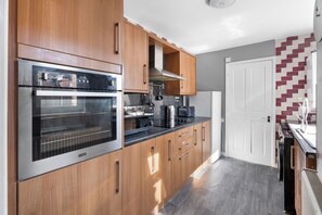 A modern kitchen with wooden cabinets, stainless steel appliances, and a tiled backsplash. - Sommerset Cottages (Sunderland)