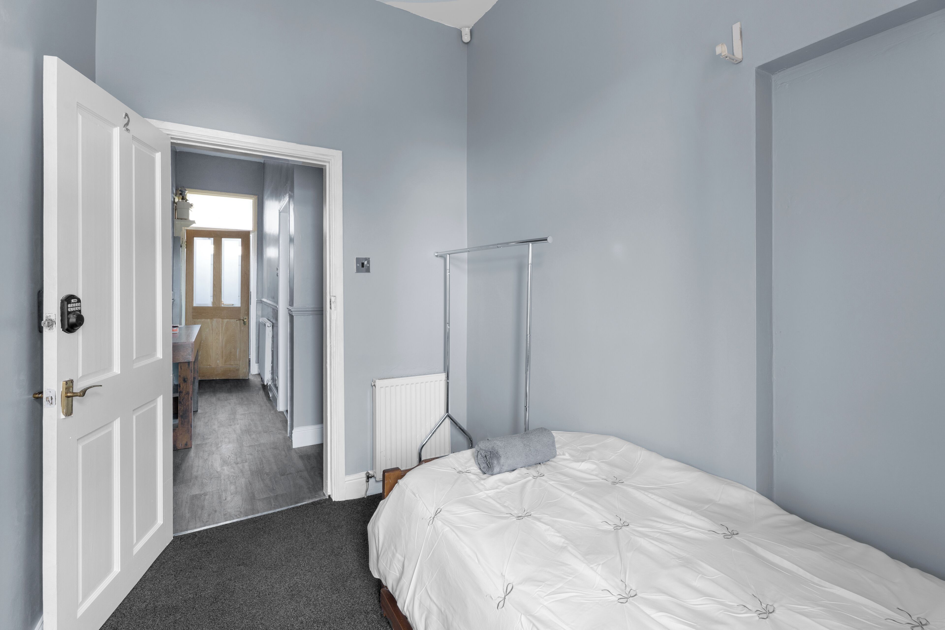 A bedroom with a bed, a radiator, a towel, and a door leading to another room.