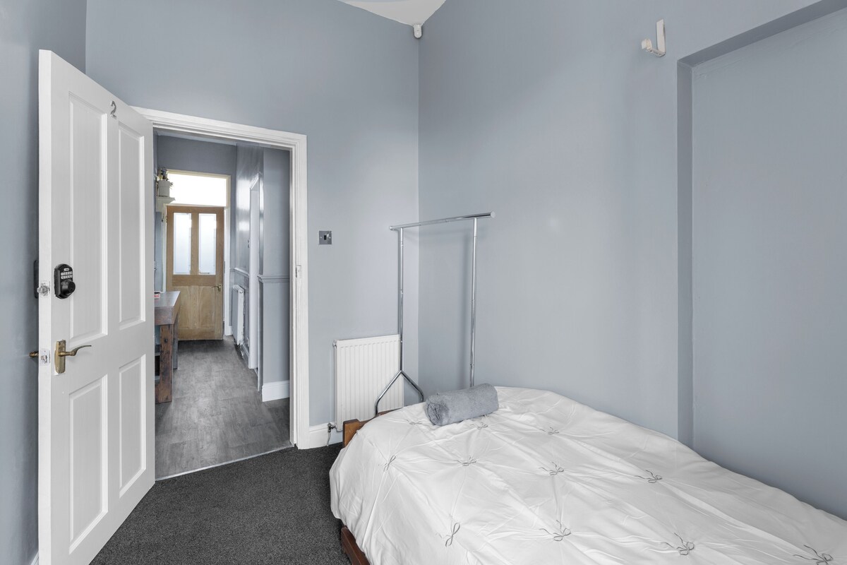 A bedroom with a bed, a radiator, a towel, and a door leading to another room.