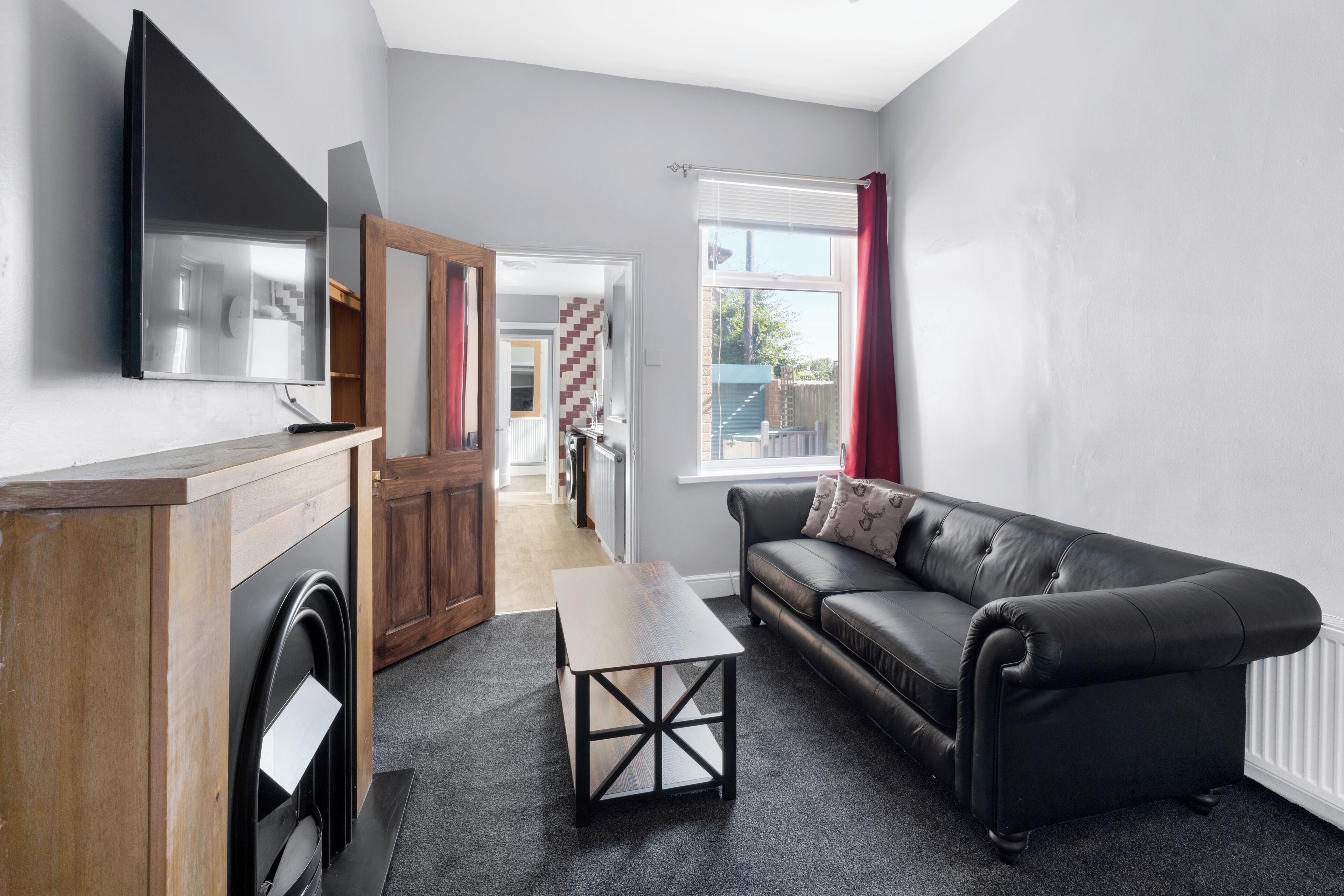 A modern living room with a black leather sofa, a wooden coffee table, and a flat-screen TV mounted on the wall.