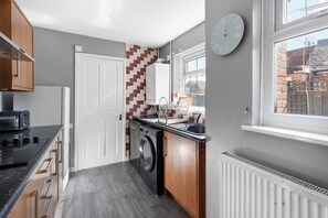 A compact kitchen with a washing machine, a sink, and a clock on the wall. - Sommerset Cottages (Sunderland)