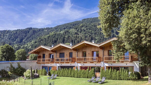 Een houten chalet met balkon, omringd door een verzorgde tuin en een bosrijk berglandschap.