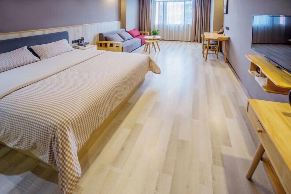 Habitació d'hotel amb un llit gran, un sofà, una taula rodona petita, una televisió i un escriptori de fusta.