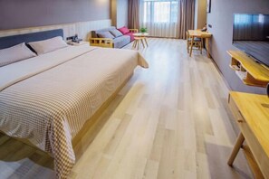 Habitació d'hotel amb un llit gran, un sofà, una taula rodona petita, una televisió i un escriptori de fusta.
