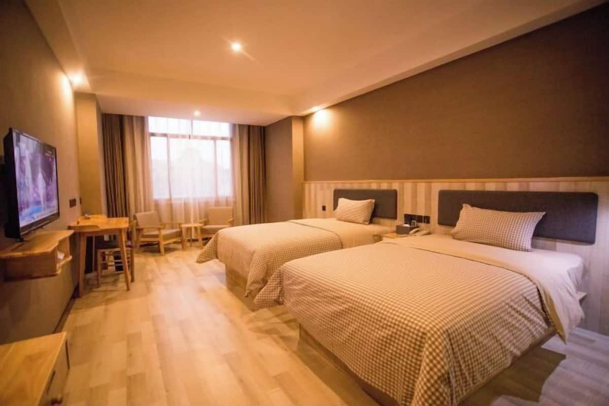 Hotellihuone, jossa on kaksi sänkyä, työpöytä, televisio ja ikkuna, jossa on verhot.