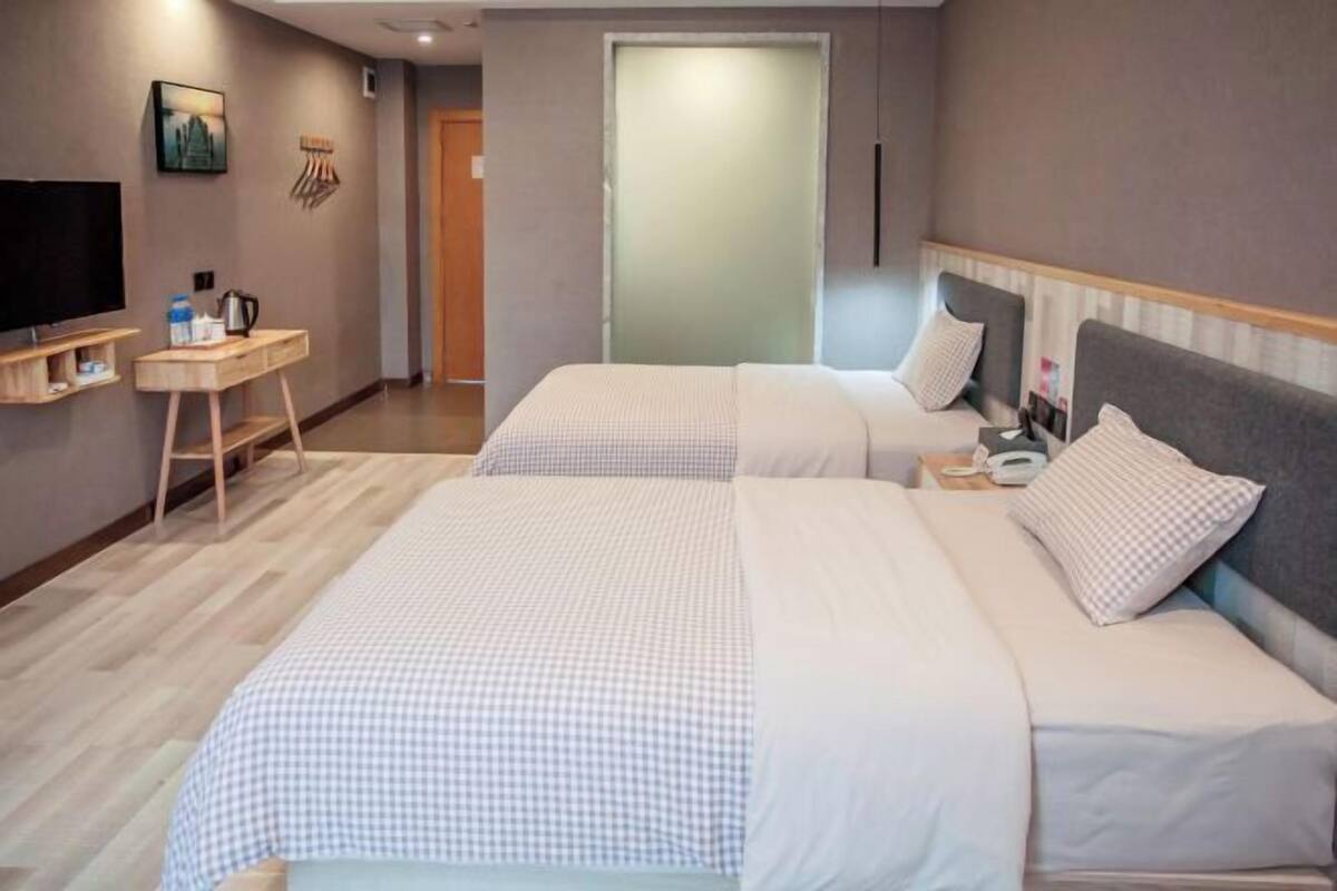 Hotellihuone, jossa on kaksi sänkyä, televisio, pieni pöytä, jossa on vedenkeitin, ja ovi, joka johtaa toiseen huoneeseen.