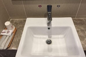 A white bathroom sink with a modern faucet, a cup, and a tissue box on the counter.