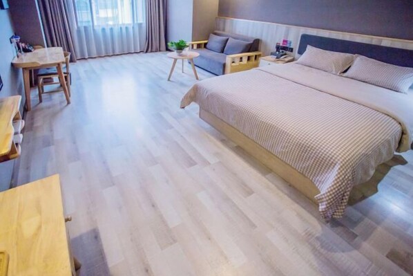 Habitació d'hotel amb un llit gran, una taula petita, un sofà i una finestra amb cortines.