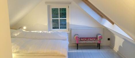A bedroom with a bed, a window, a radiator, and a bench.