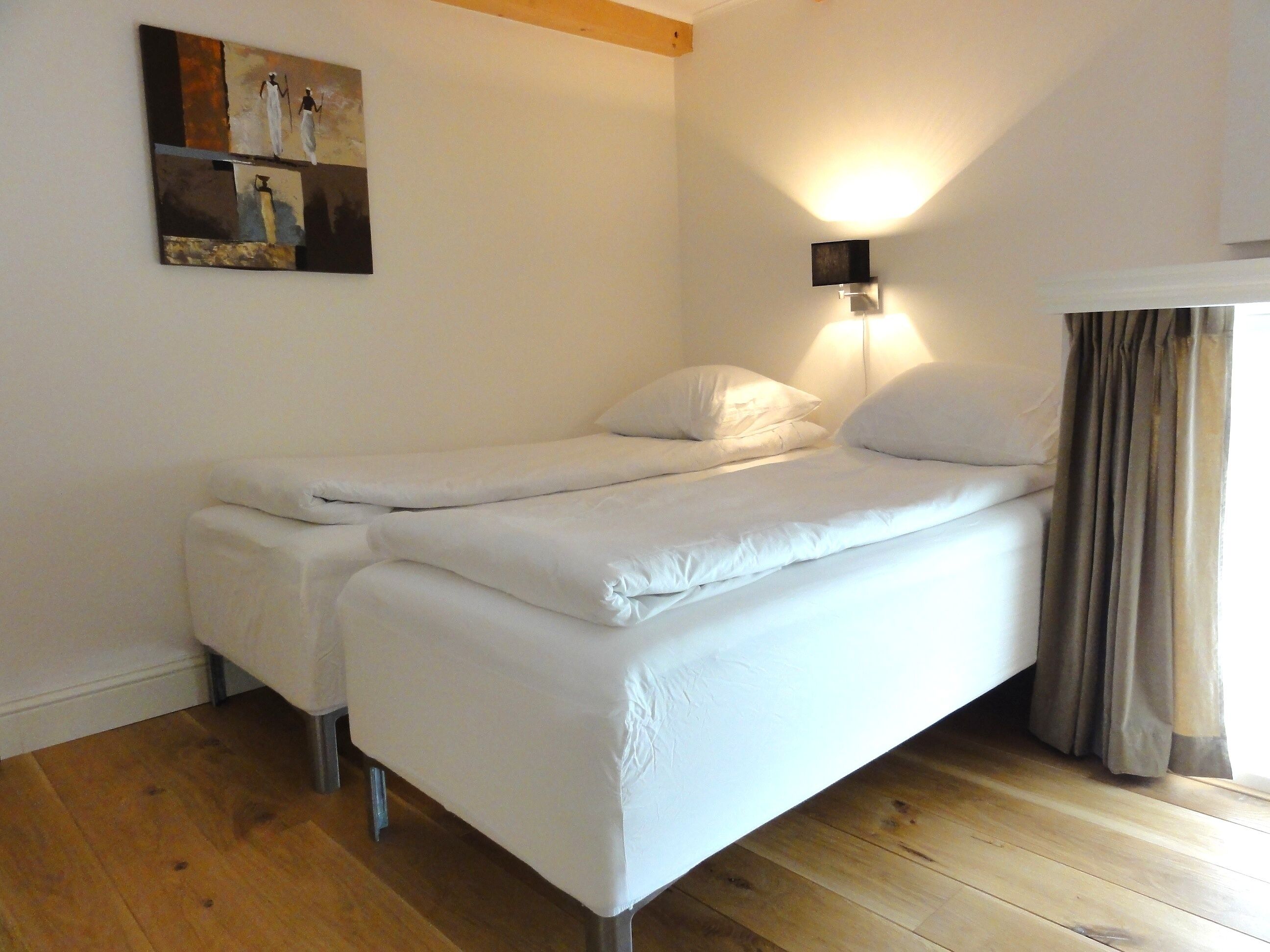 Ein Einzelbett mit weißer Bettwäsche in einem Zimmer mit Holzboden und einer an der Wand befestigten Leuchte.