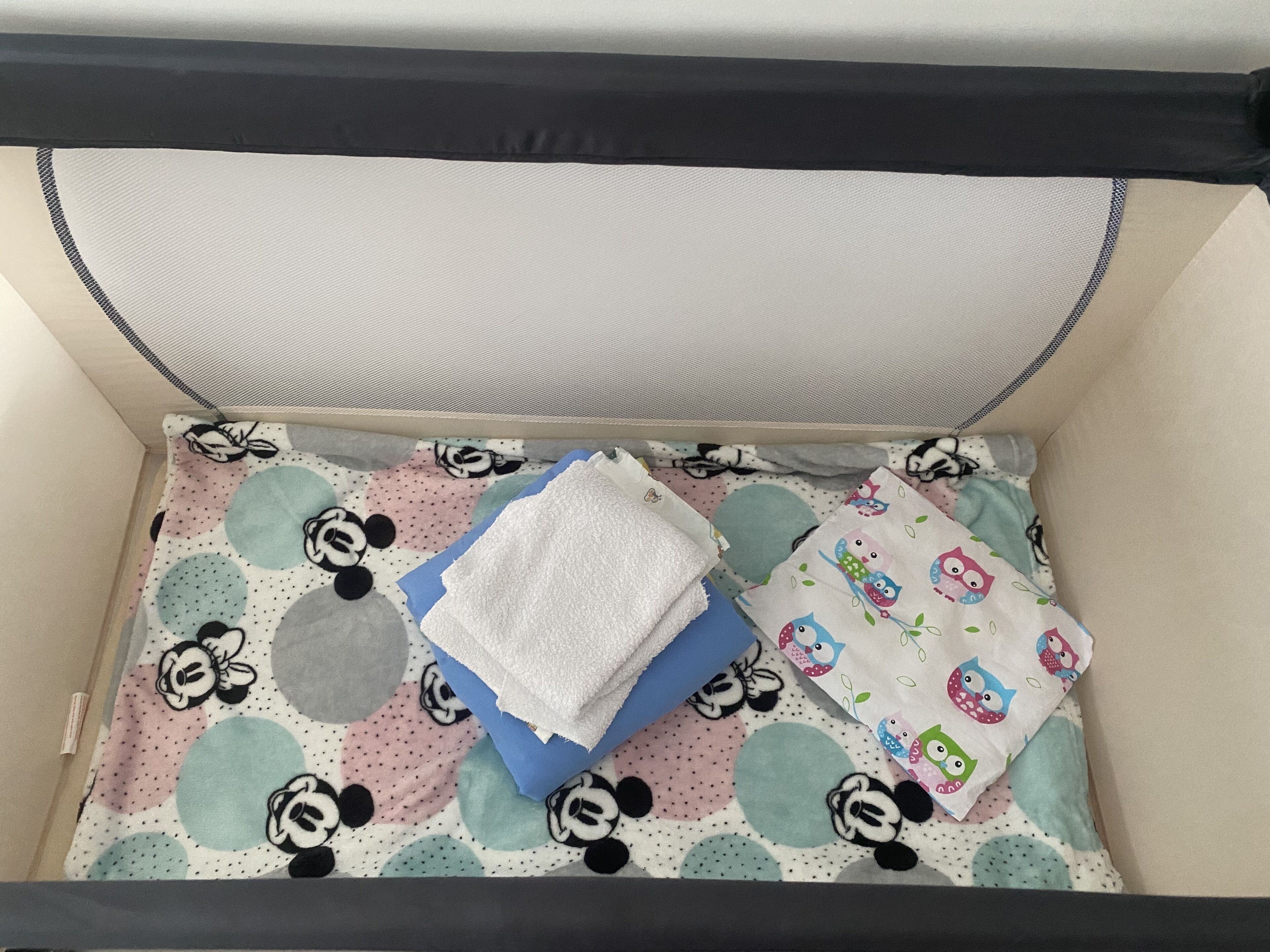 Una cuna con un colchón con temática de Mickey Mouse, una manta azul y una toalla blanca.