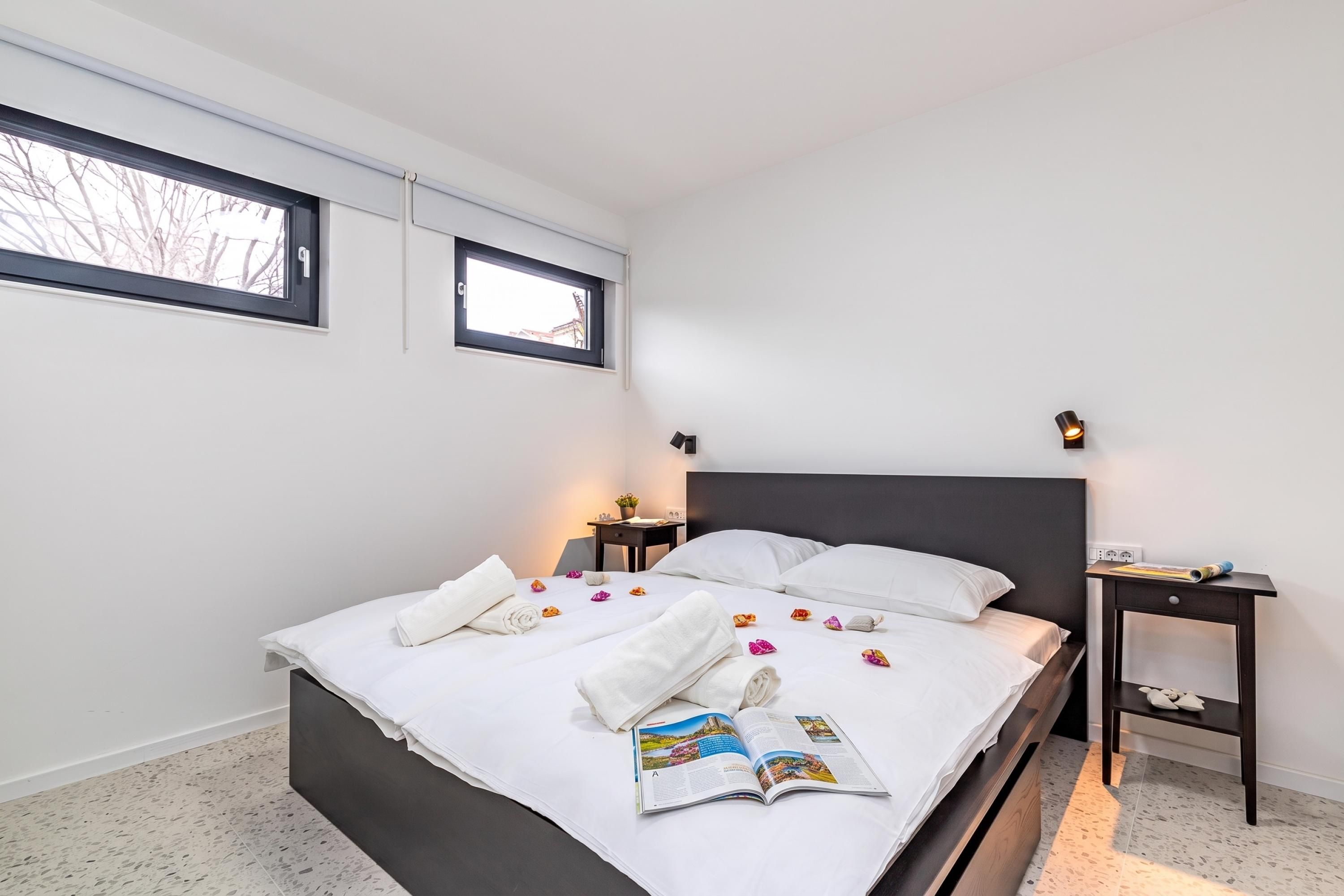 A modern hotel room with a large bed, two bedside tables, a window, and a magazine on the bed.
