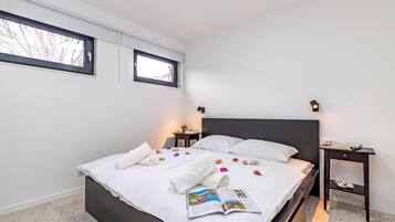 A modern hotel room with a large bed, two bedside tables, a window, and a magazine on the bed.