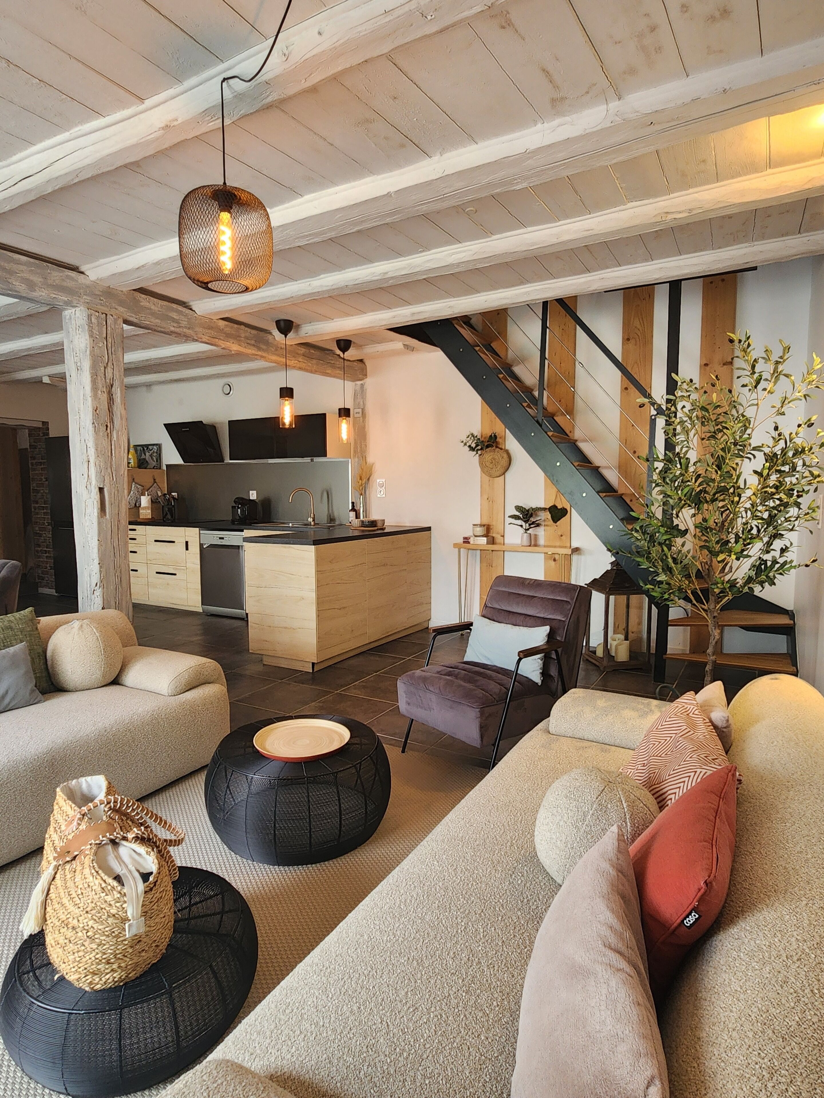 Un salon moderne avec un canapé, un pouf et un escalier menant à une cuisine.