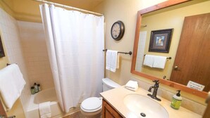 A bathroom with a bathtub, toilet, sink, and a mirror with a clock. - Trapper Condo Unit 3 (West Yellowstone)