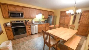 A kitchen with wooden cabinets, a stainless steel microwave, a stove, a dishwasher, and a dining table with chairs. - Trapper Condo Unit 3 (West Yellowstone)