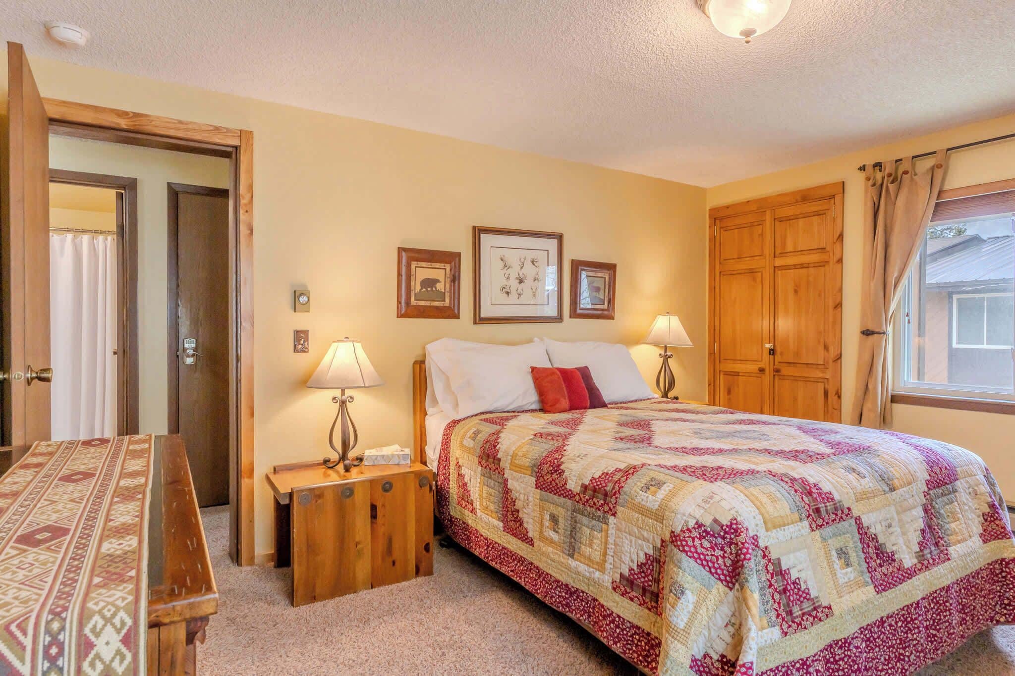 A bedroom with a bed, two bedside tables, a wooden bench, a door, and a window with curtains.
