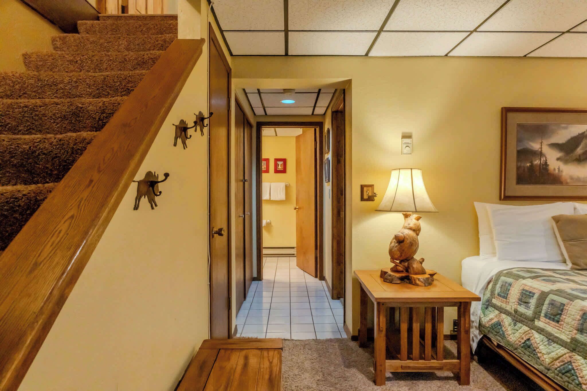 Une chambre d’hôtel avec un escalier en bois, un couloir menant à une salle de bain, une table de chevet avec une lampe et un lit recouvert d’une courtepointe.