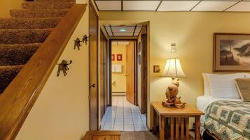 Une chambre d’hôtel avec un escalier en bois, un couloir menant à une salle de bain, une table de chevet avec une lampe et un lit recouvert d’une courtepointe.