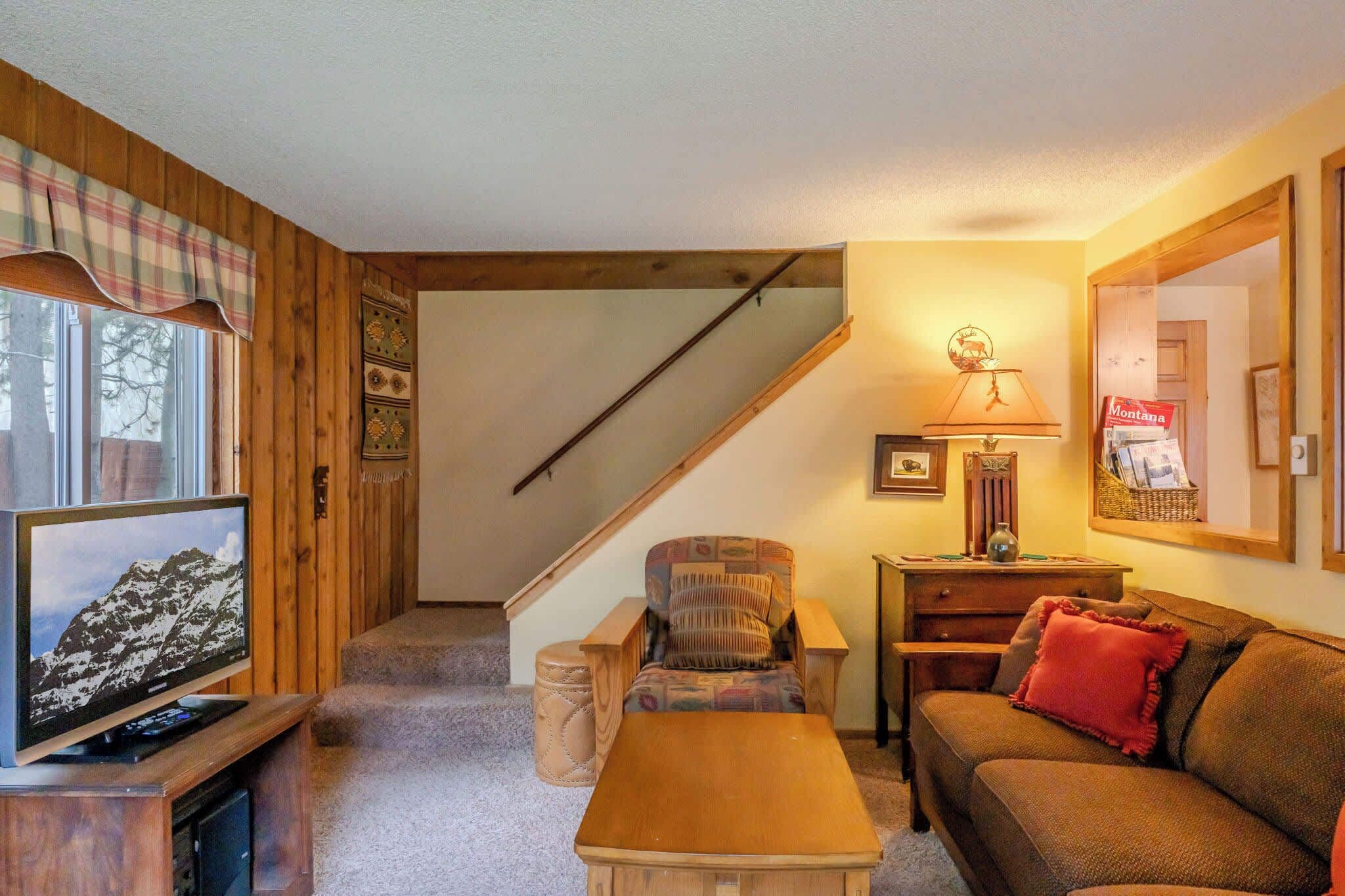 A cozy living room with a television, a sofa, a chair, a table, and a lamp.