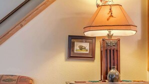 Une pièce chaleureuse avec un escalier en bois, un lit recouvert d’une couverture à motifs, une commode en bois ornée d’un vase et un tableau encadré accroché au mur.