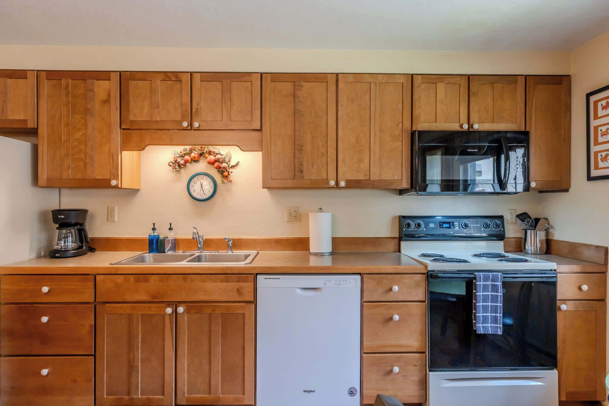 A kitchen with wooden cabinets, a stainless steel sink, a dishwasher, a stove, and a microwave.