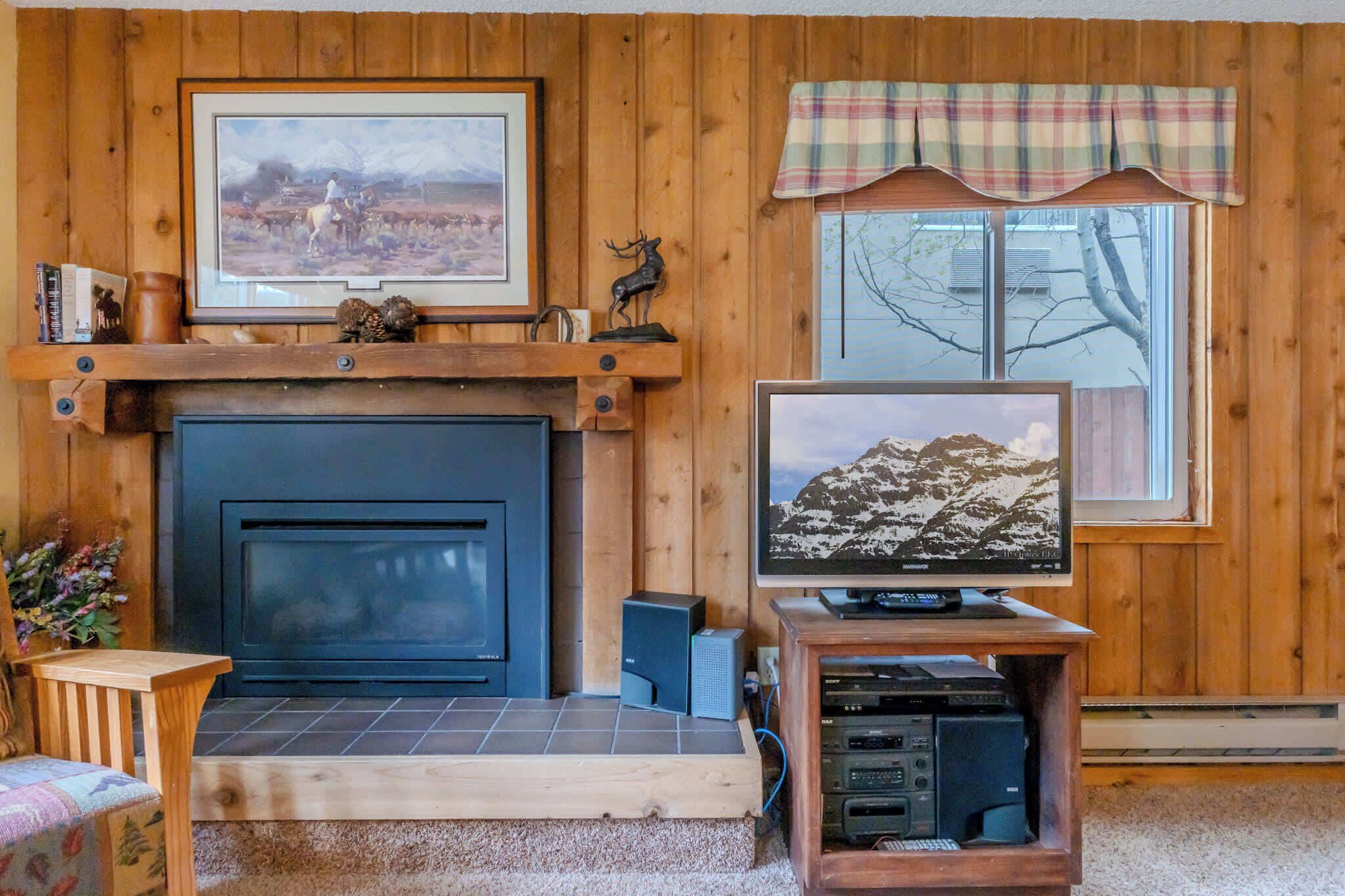 A living room with a fireplace, a mounted television, and a window with a plaid valance.